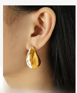 Gros plan de boucles d'oreilles goutte en métal doré et émail blanc quadrillé
