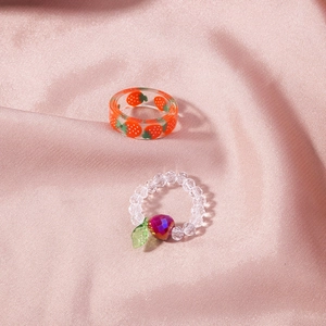 Detailed macro of crystal strawberry ring and resin band on pink satin fabric