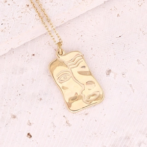 Macro view of golden rectangular pendant with an abstract face relief on a stone base
