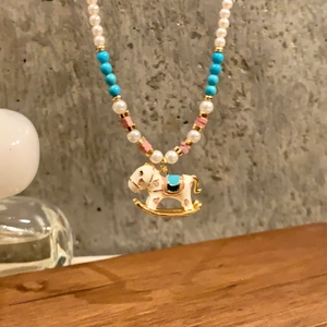Detail view of a pearl necklace with turquoise beads and a white enamel rocking horse pendant
