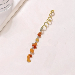 Close-up of golden spiral hair coil with natural orange stone pendant on marble background