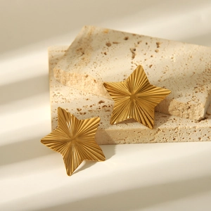 Detail of gold star earrings with radial texture on a beige travertine stone block