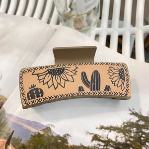 Minimalist beige rectangular hair claw with black sunflower and cactus prints on magazine