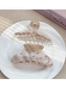 Close-up of beige acetate hair claws with rhinestones on a ceramic plate background