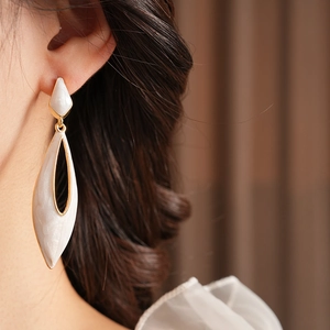 Close-up of vintage teardrop earrings with white enamel and elegant gold frame on model