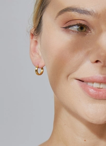 Close-up of small gold round hoop earrings with textured finish worn by a model