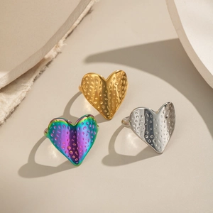 Trois bagues cœur texturées en or, argent et fini iridescent sur un fond minimaliste