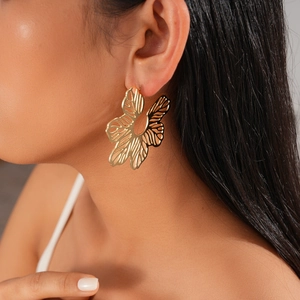 Close-up of golden hollowed flower earrings with brushed metal texture for women