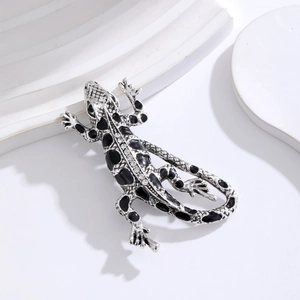 Detailed close-up of a silver lizard brooch with black enamel and sparkling rhinestones