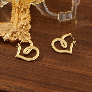 Minimalistische herzförmige 18K vergoldete Ohrstecker auf einem Vintage-Holzhintergrund