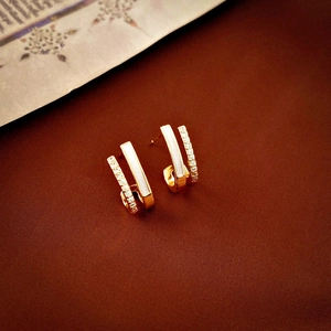 Detail of gold geometric earrings with white inlay and shimmering zircons on dark background
