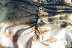 Close-up of pleated tie-dye fabric in dark green and ochre for long dress set