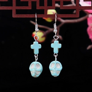 Detail of turquoise skull and cross earrings hanging on a vintage wooden lattice background