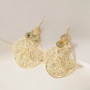 Close-up of golden bohemian drop earrings with layered hollow floral and geometric patterns