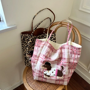 Detail of dachshund embroidery on leopard and pink plaid canvas tote bags on a wooden chair