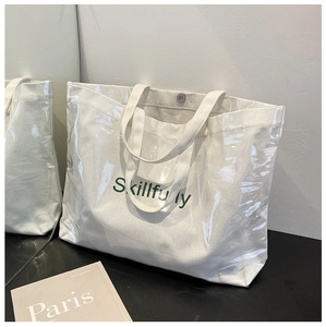Detail of white canvas and transparent PVC tote bag with green Skillfully lettering print