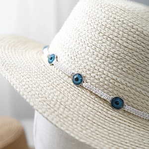 Detail of cream straw hat featuring blue evil eye charms on a woven white band