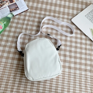 Détail d'un sac bandoulière blanc en PU sur fond quadrillé avec sangle tissée et boucle