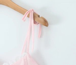 Détail d'une robe rose avec dentelle blanche et bretelles à nouer sur un cintre en bois naturel