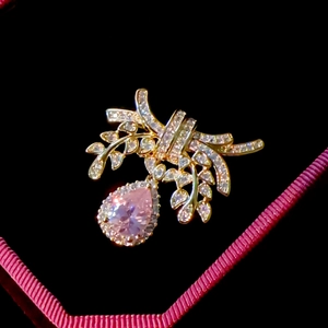 Elegant gold bow brooch with sparkling crystals and a large pink teardrop gemstone