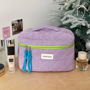 Close-up of quilted purple checkered makeup bag with green zipper and blue tassels