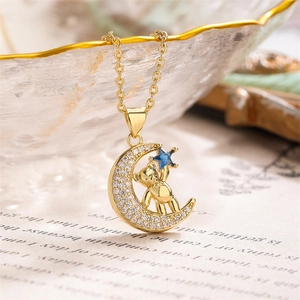 Macro detail of a gold bear and zircon moon pendant on a delicate chain over a glass bowl