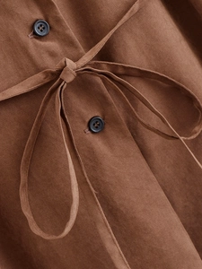 Detailed close-up of brown linen fabric texture with dark buttons and adjustable belt