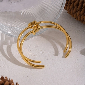 Eleganter doppelreihiger Knotenarmreif aus goldfarbenem Edelstahl auf weißem Stein