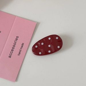 Detailed view of a red oval hair clip with white polka dots on a minimalist background