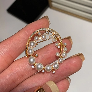 Handheld view of a 24k gold plated round brooch with sparkling zircons and pearls