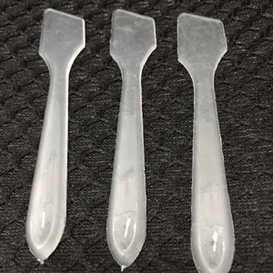 Three translucent plastic beauty spatulas for face masks and creams on a mesh background