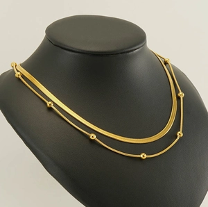 Detail of double-layer gold snake chain and beaded necklace on a black mannequin