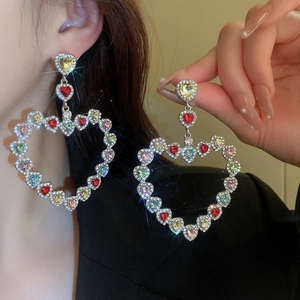 Detailed view of oversized colorful rhinestone heart earrings on model with sparkling effect