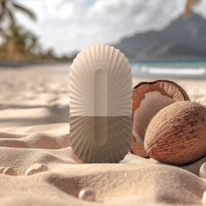 Close-up of a brown ice roller on beach sand next to a coconut for cooling skincare
