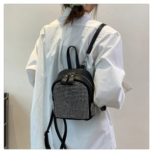 Detail of black mini backpack with silver rivets and dual handles worn on white shirt