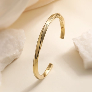 Polished 18K gold plated minimalist twisted rope cuff bracelet on a white stone background