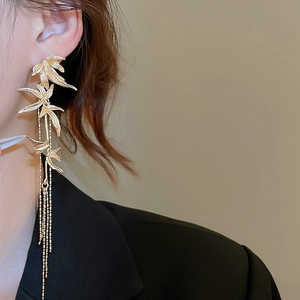 Detail shot of golden bamboo leaf tassel earring worn by a model on plain background