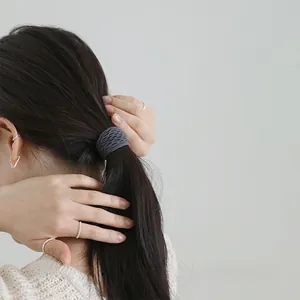 Close-up of a dark grey woven elastic hair tie worn on a ponytail with silver jewelry