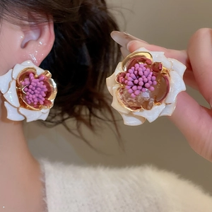 Détail de la boucle d'oreille fleur en émail blanc avec bords dorés portée à l'oreille