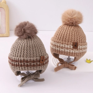 Close-up of two knit baby hats with pom-poms, earflaps, and Kuk leather tags