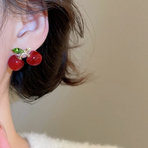 Close-up of model wearing small cherry stud earrings with red fruits and green leaves