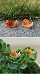 Macro detail of miniature resin snails with orange shells for succulent garden landscape