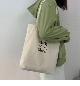Primer plano de bolso de lona beige con estampado de ojos shh! usado por modelo