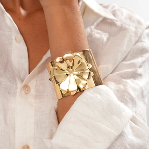 Gros plan d'un bracelet manchette doré large avec détail de fleur 3D polie