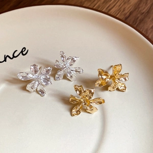 Close-up of gold and silver metallic flower earrings with textured 3D petals on a tray