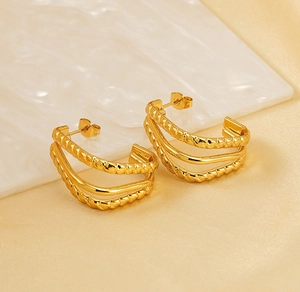 Close-up of golden multi-layer twist and smooth hoop earrings on marble display
