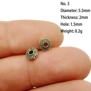Macro shot of 5.5mm silver flower spacer beads on fingertip for DIY jewelry making