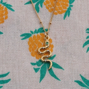Golden snake pendant necklace with clear crystals and green eyes on fabric background