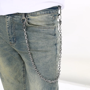 Close-up of a silver Cuban link pant chain with a detailed skull charm on denim jeans