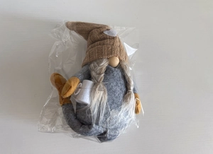 Detail of plush Christmas gnome with knitted heart hat and braids in clear packaging